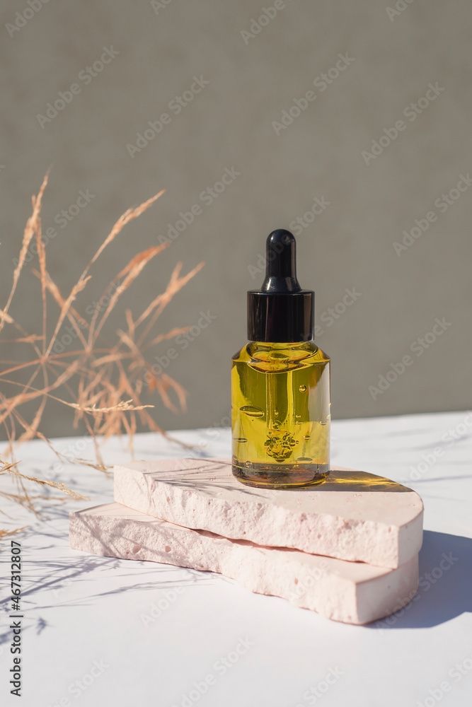 Green glass dropper bottle with black lid on a podium with dry plants on light background. Skincare products , natural cosmetic. Beauty concept for face and body care