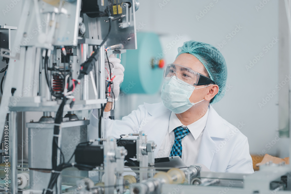 Both male and female Asian scientists are outfitted with protective gear. Examining the factory's machinery and materials used in the mask-making process. Covid 19 is a piece of preventive equipment.
