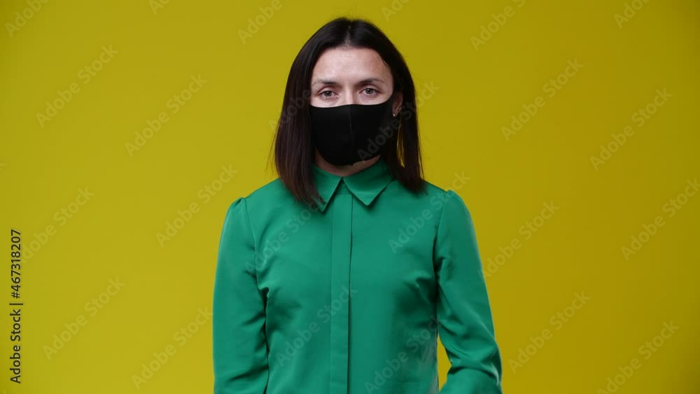 the girl puts on a protective mask on her face, she is without emotion, looks at the camera, brunette, short hair, dressed in a green T-shirt, the background is yellow the girl puts on a protective mask on her face, she is without emotion, looks at the camera, brunette, short hair, dressed in a green T-shirt, the background is yellow
