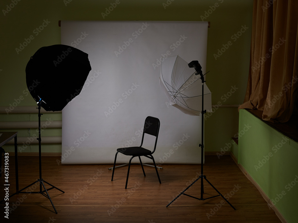 The chair is standing next to the white one, she is next to the lighting equipment