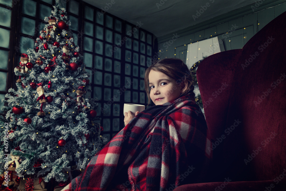 A little girl with pigtails drinks tea from a white mug wrapped in a tart plaid