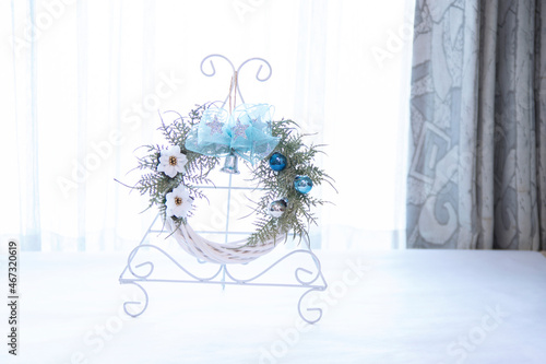 リース台に飾った星模様の青いリボンと白のポインセチアのクリスマスリース（窓辺）