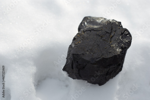 The black coal stone lying on the white snow symbolizes energy, warmth and wealth