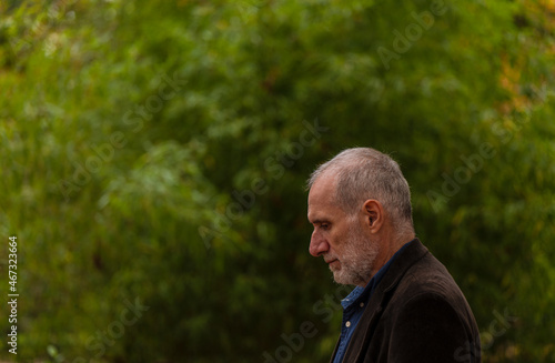 Side view of adult man in suit in public park in autumn against green plants. Shot in Retiro Park, Madrid, Spain