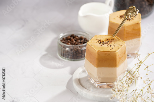 Two glasses with trendy korean beverage dalgona coffee latte - whipped instant coffee, sugar and hot water and milk layers on a marble board, white surface