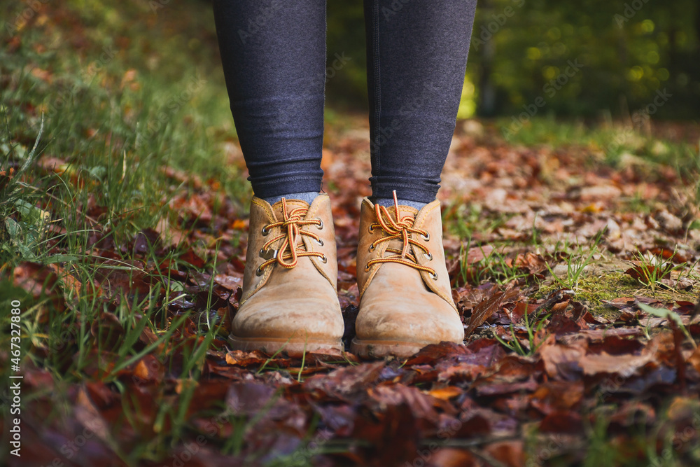 close up view of a woman legs wearing mountain boots, autumn leaves background