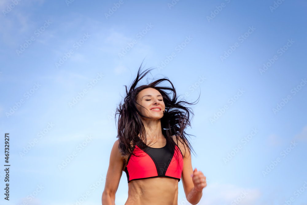Naklejka premium Attractive brunette woman in red sportswear runs against the blue sky
