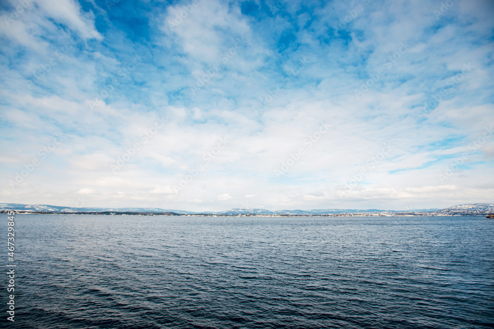 Scenic view of calm cold sea fjord with shore and mountain hills on the background