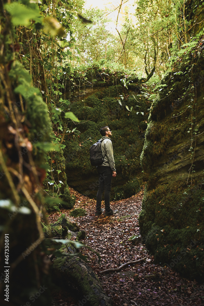 young man backpacker walking through rock walls in the middle of a forest, forest landscape, natural moss walls