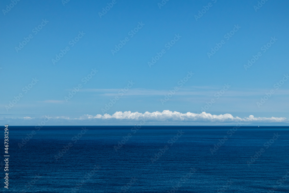 Blue Ionian sea landscape and skyscape view in Greece. Bright day with low scenic white clouds over dark deep blue water surface