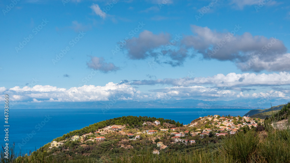 Scenic vibrant traditional greek village with orange tiled roofs on green hills near blue sea shore on Lefkada island, Greece. Travel Europe in summer