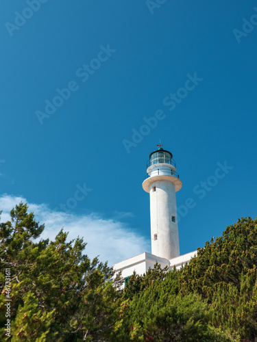 White lighthouse tall tower in pine bushes greenery on vivid blue sky in Greece, Ionian sea. Scenic travel destination. Lefkada island. Vertical