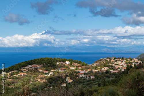 Fototapeta Naklejka Na Ścianę i Meble -  Picturesque traditional greek village with orange tiled roofs on green hills near blue sea shore on Lefkada island, Greece. Travel Europe in summer