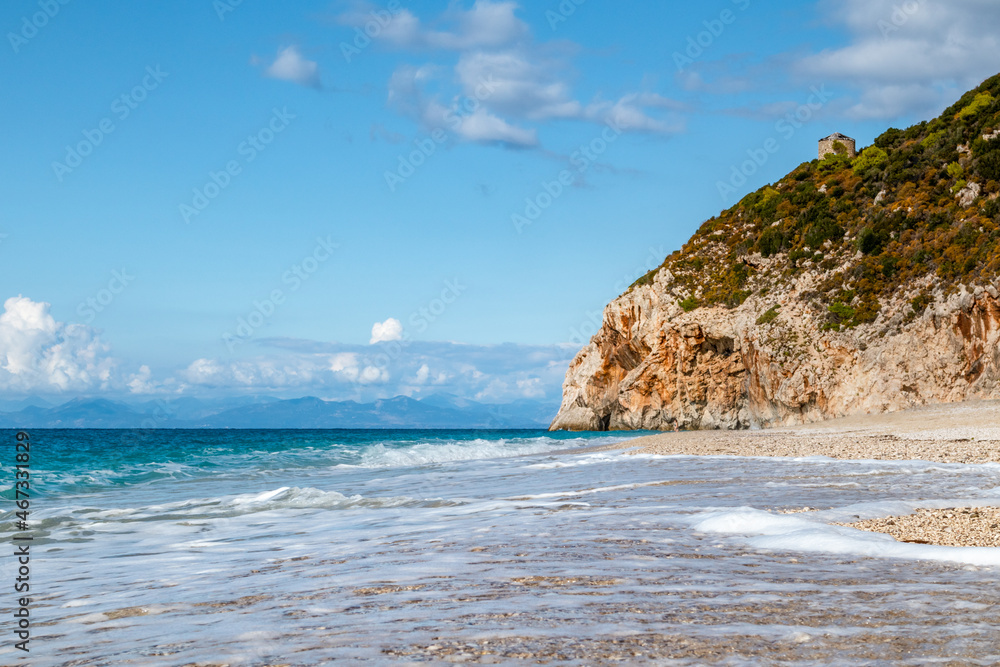 Mylos sandy beach with azure stormy waves and white foam in vivid sunset light on coast of Lefkada island in Greece. Summer nature vacation travel to Ionian Sea