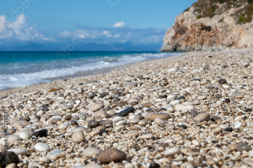 Mylos beach white wet shiny pebble stones close-up with azure sea, stormy waves, epic clouds and rocky cliff on coast of Lefkada island in Greece, Ionian Sea