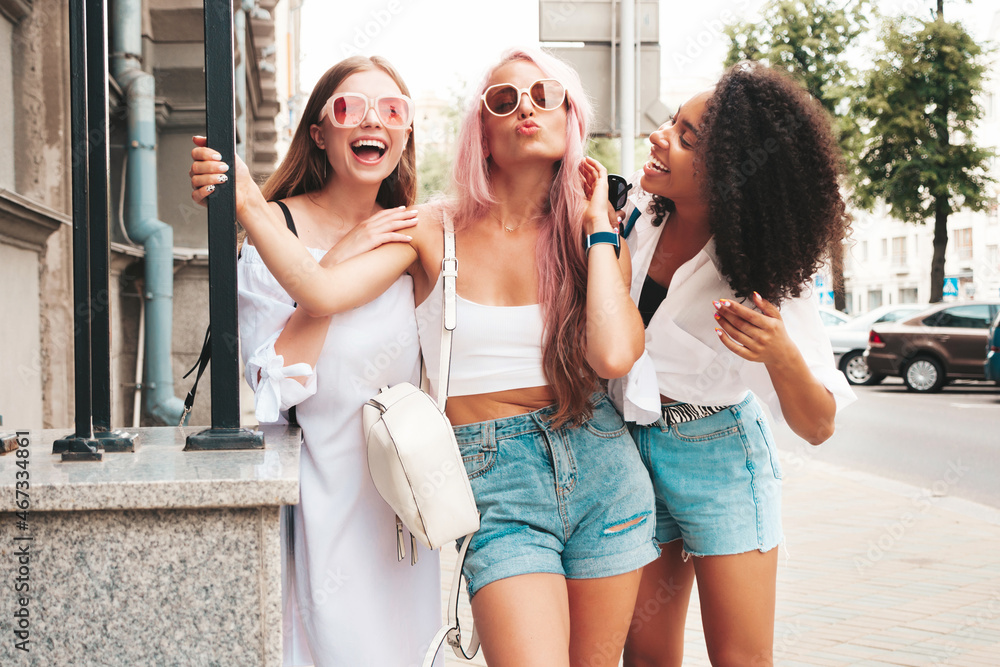Three young beautiful smiling female in trendy summer clothes.Sexy carefree multiracial women posing on the street background.Positive models having fun in sunglasses. Cheerful and happy