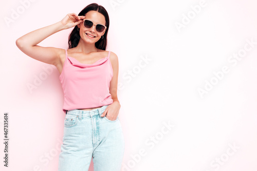 Closeup portrait of young beautiful smiling female in trendy summer clothes. Sexy carefree woman posing near pink wall in studio. Positive model having fun indoors. Taking off sunglasses