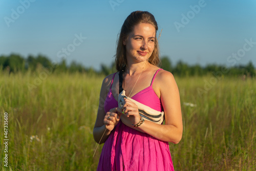 A girl in a pink dress stands in the field