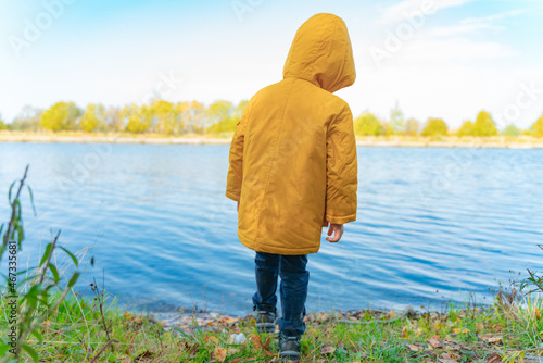 A boy in a yellow jacket stands near the lake
