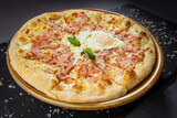 Italian bacon pizza with egg and cheese sauce, wooden dish plate on a stone table top.