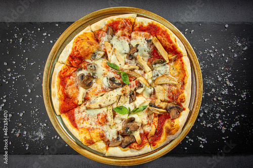 Pizza with chicken and mushroom. wooden dish plate on a stone table top.