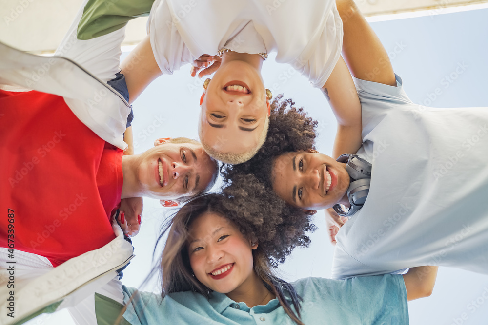 Low angle view of multiethnic young trendy friends hugging, smiling and making a circle with their heads. Low angle view of multiethnic young trendy friends hugging, smiling and making a circle with their heads.