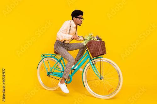 Full length body size photo man riding bike with flowers basket in glasses isolated vivid yellow color background