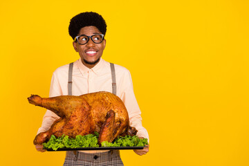 Photo of cheerful guy hold dish baked turkey look empty space wear specs suspenders shirt isolated yellow color background