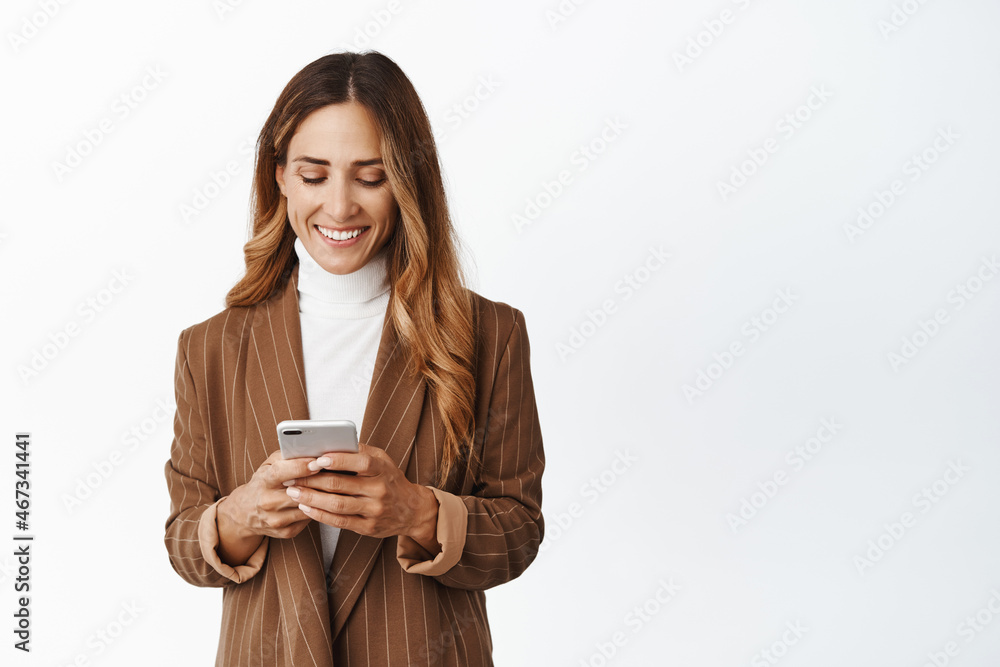 Smiling corporate woman order taxi in app, chatting in messanger app on smartphone, looking at her phone screen with pleased face, white background Smiling corporate woman order taxi in app, chatting in messanger app on smartphone, looking at her phone screen with pleased face, white background