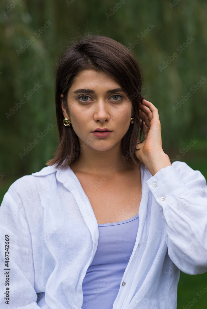 Attractive, happy and stylish brunette Caucasian girl posing in a park in nature. Lifestyle and fashion concept. Attractive, happy and stylish brunette Caucasian girl posing in a park in nature. Lifestyle and fashion concept.