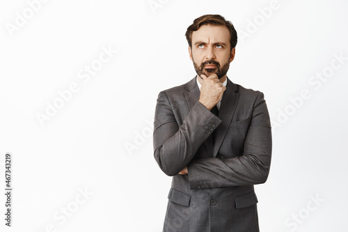 Thoughtful boss in suit, looking at upper left corner, furrow eyebrows while thinking, making serious choice, white background