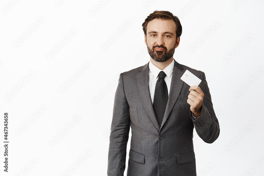 Upset businessman showing credit card and grimacing, standing over white background Upset businessman showing credit card and grimacing, standing over white background