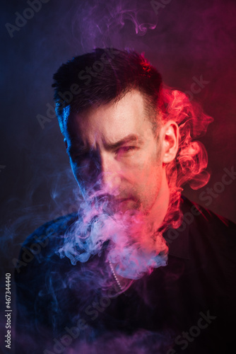 portrait of a serious young man inhaling smoke in multicolored light