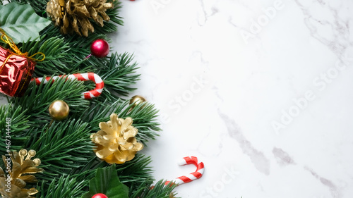 Green pine tree leaves  red christmas decorations and candy canes on white marble background  christmas decorations in bright red color. Simple and creative christmas concept.