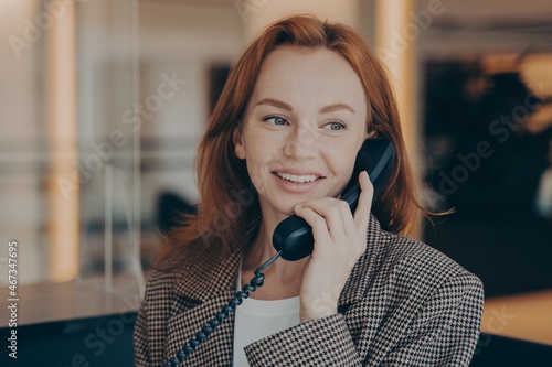 Portrait of satisfied female office worker using black landline phone, calling business partner photo
