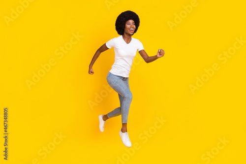 Full length photo of pretty sweet dark skin lady wear white t-shirt jumping high running fast smiling isolated yellow color background © deagreez