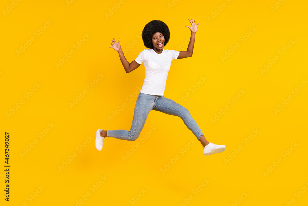 Full length photo of charming funky dark skin lady wear white t-shirt jumping high isolated yellow color background Full length photo of charming funky dark skin lady wear white t-shirt jumping high isolated yellow color background