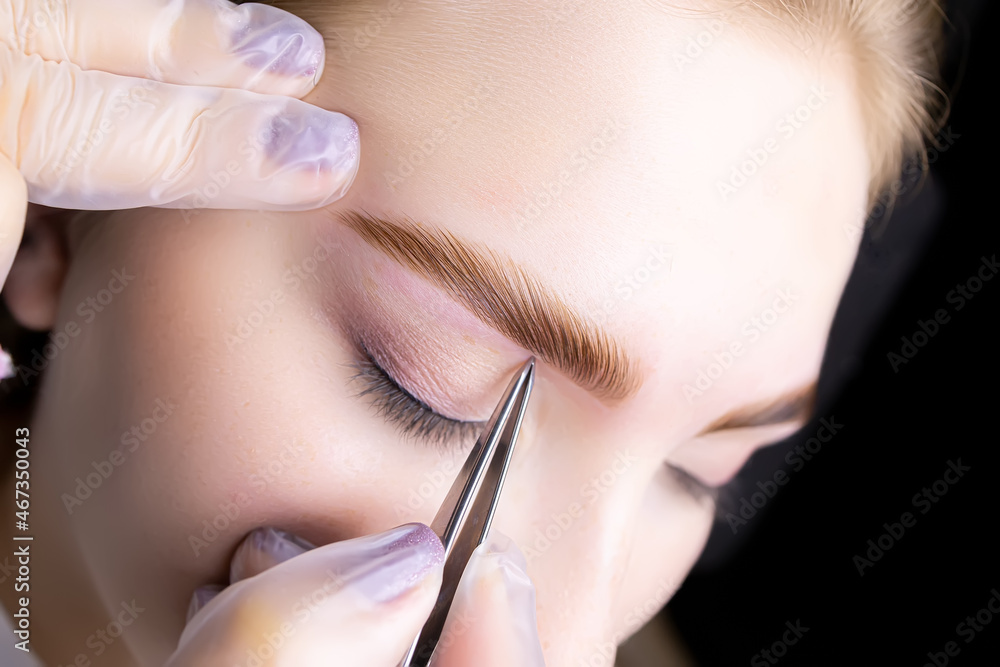 the hands of a close-up master who stretches the tail of the eyebrows and removes excess hairs with tweezers