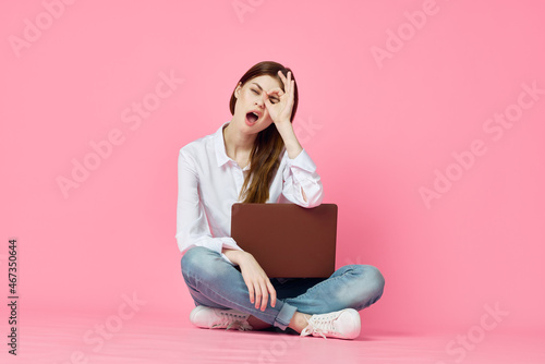 cheerful woman with laptop sitting on the floor on a pink background
