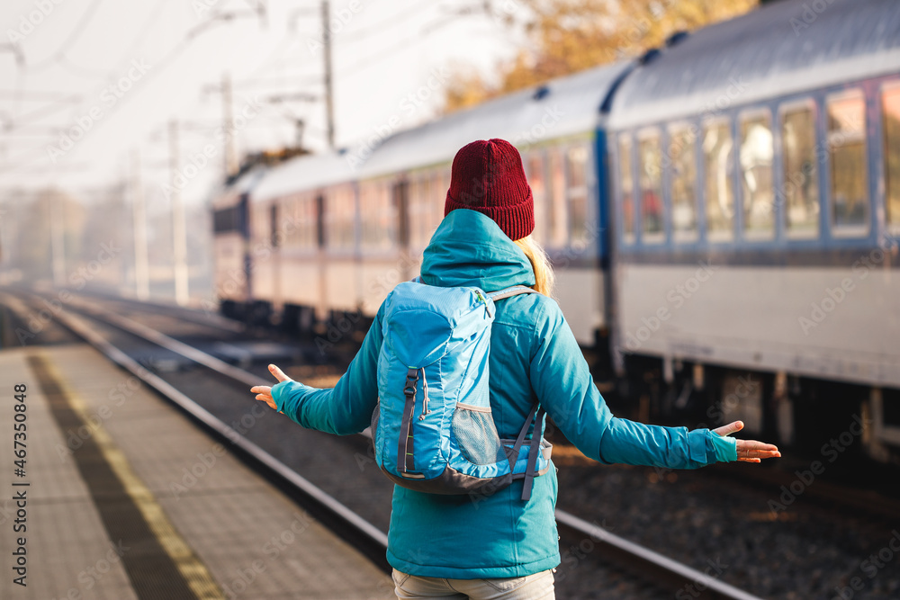Obraz premium Confused tourist standing at wrong railway station platform. Disappointment during traveling. Woman with backpack looking at leaving train. Solo traveler
