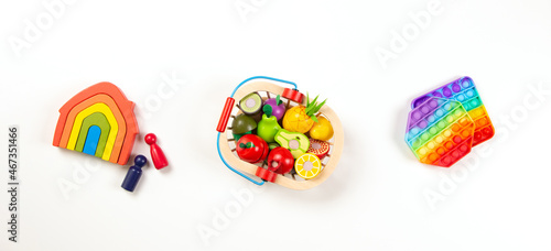 Baby kids toys. Top view to colorful toys arranged on white background. Wooden rainbow house, wooden fruit and vegetables and pop it toys. Leisure entertainment and education for children