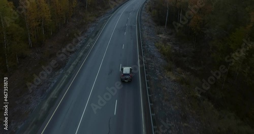 One gray silver crossover SUV car driving alone road trip, travel on freeway through dense colorful forest corridor at autumn sunny sunset - Aerial drone wide view