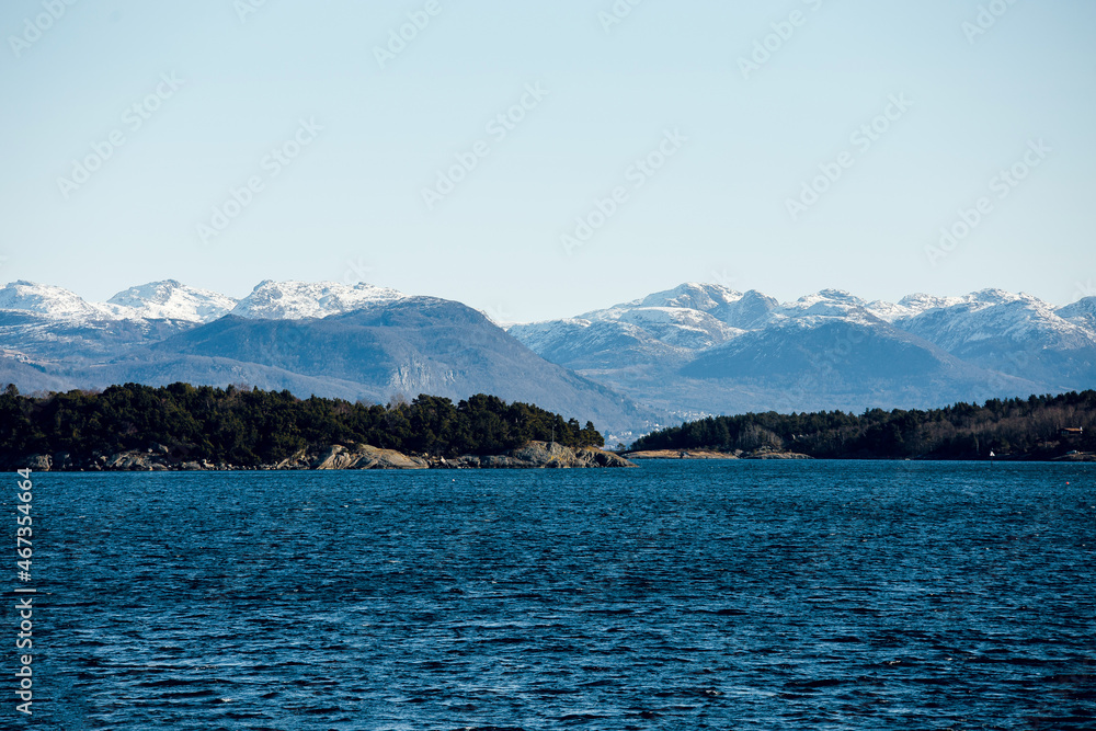 Beautiful scenic view of cold blue sea, island with stony shore and mountains with snowy peaks on the background