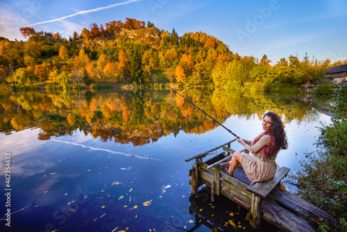 a young and elegant woman who fishes on the shore of a lake in the autumn season