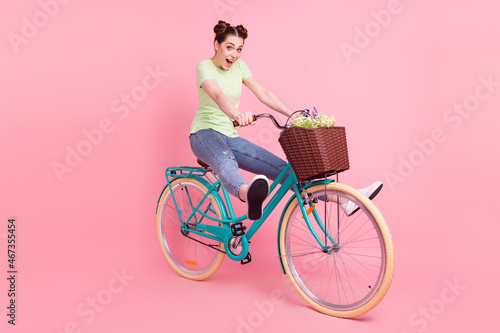 Photo of excited sporty lady drive bicycle have fun open mouth wear green t-shirt isolated on pink background © deagreez