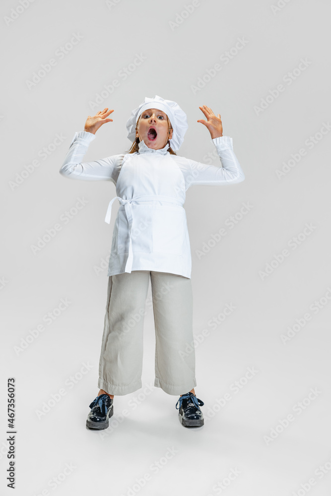 Portrait of little cute girl in white cook uniform and huge chef's hat standing isolated on white studio background. Portrait of little cute girl in white cook uniform and huge chef's hat standing isolated on white studio background.