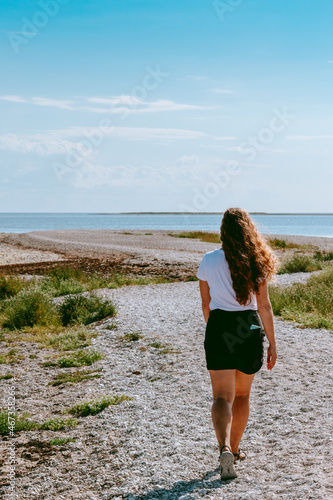 Woman with long brown curly hair walking by the coast of the Baltic sea in Sorve peninsula in Saaremaa, Estonia during sunny and calm day