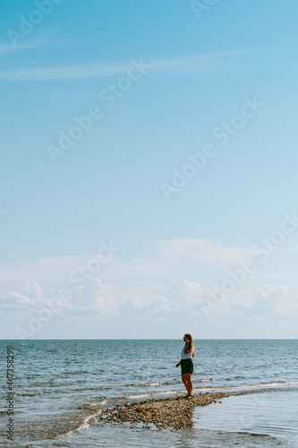 Woman with long brown curly hair walking by the coast of the Baltic sea in Sorve peninsula in Saaremaa, Estonia during sunny and calm day