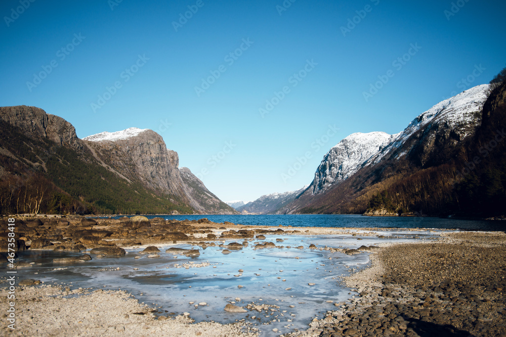Beautiful view of rocky sea shore and beautiful mountains with snow peaks. Stony river bank