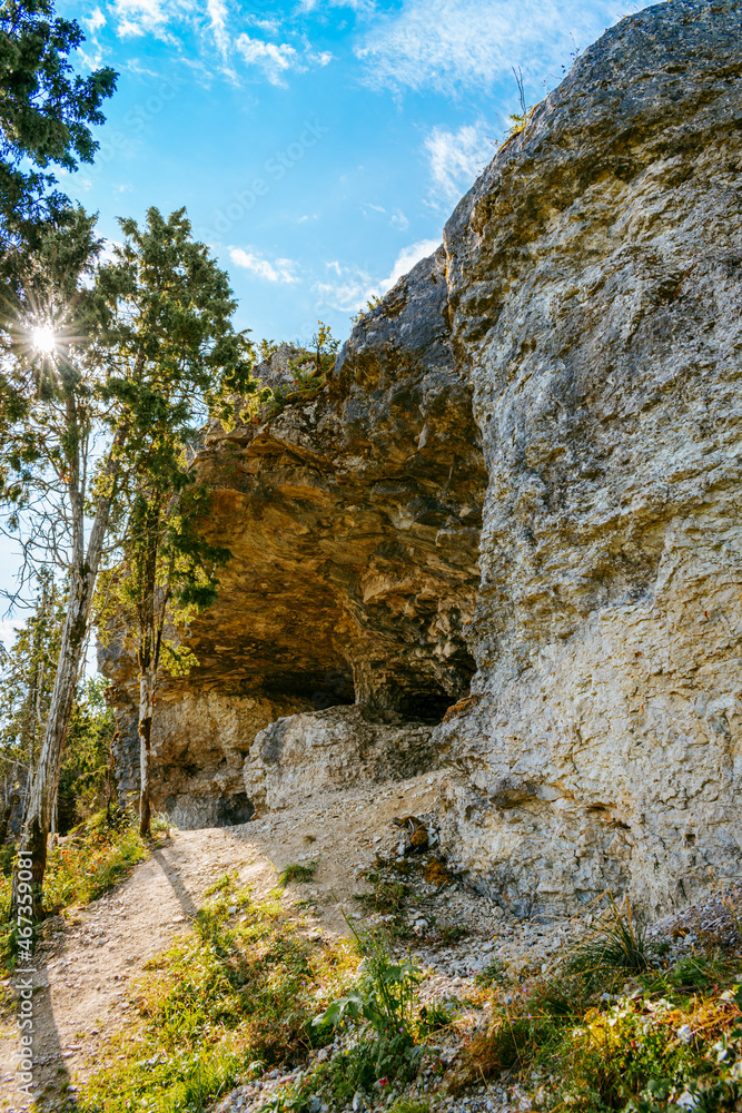 Uugu bluff or cliff on the Muhu Island in Estonia, located by the Baltic sea and near the island of Saaremaa. Beautiful sunny day with blue sky, white clouds, forest and stone cliffs by the seaside.